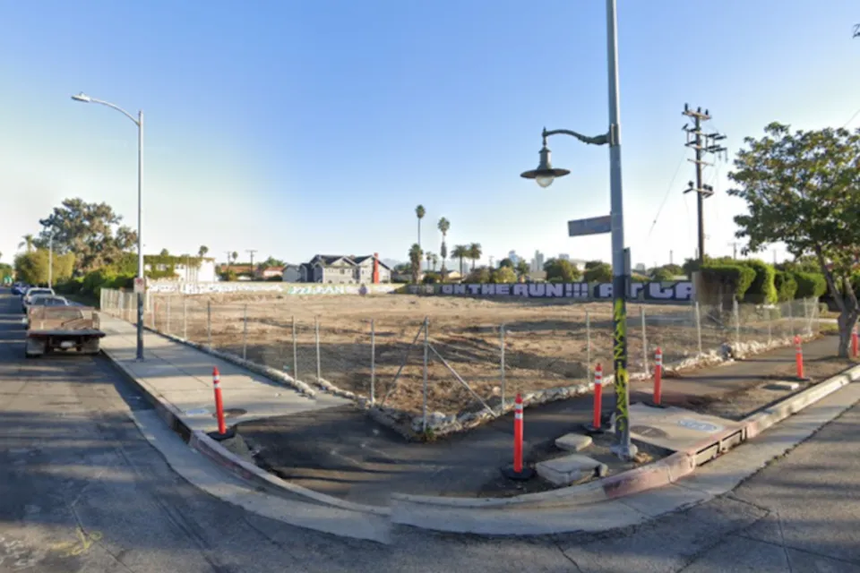 Google street view of vacant fenced-in dirt lot in South Los Angeles with graffiti on wall in background.